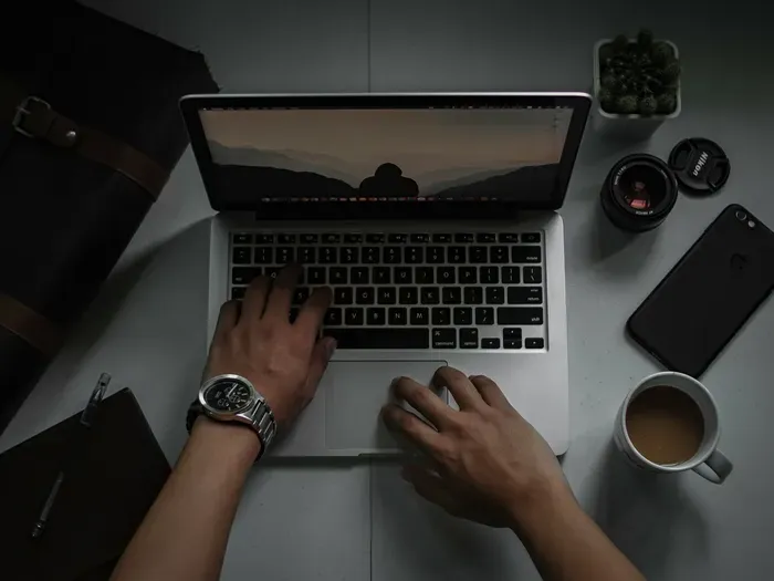 Overhead view of a person working on laptop with coffee, camera lens, and phone on desk for Town Service Network Hub